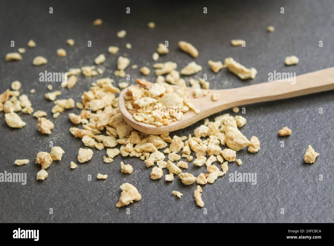 Gros plan de viande de soja séchée hachée sur une cuillère en bois sur une table grise Banque D'Images