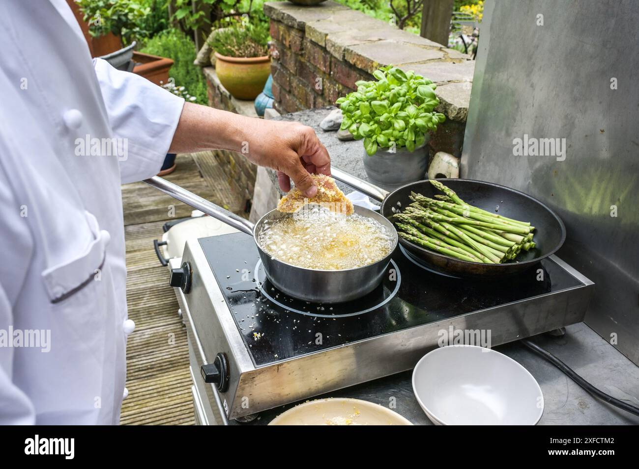 Cuire des morceaux de poulet panko panés à friture dans une casserole d'huile chaude dans une cuisine extérieure rustique, concept de cuisson d'été, foyer sélectionné, profondeur étroite de Banque D'Images