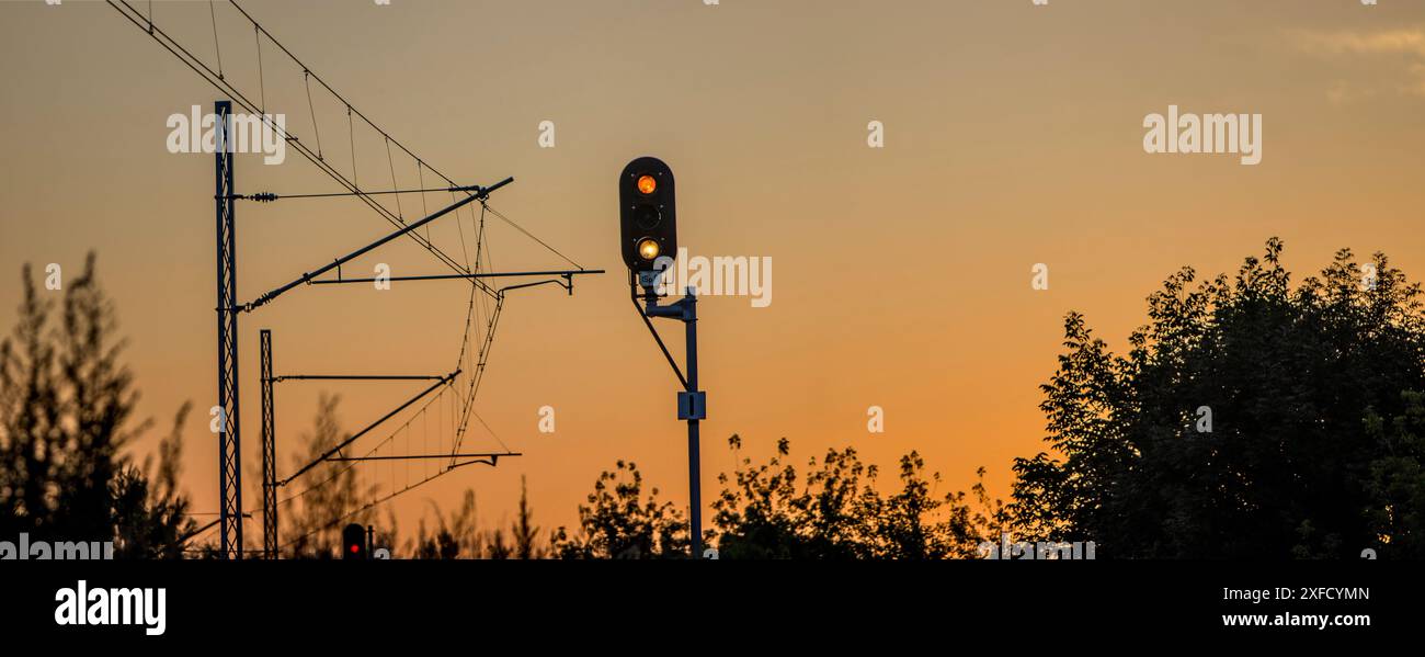 Sémaphore ferroviaire incandescent, sur fond de traction électrique pour trains. Coucher de soleil par une journée chaude. Sémaphore répété. Panorama Banque D'Images