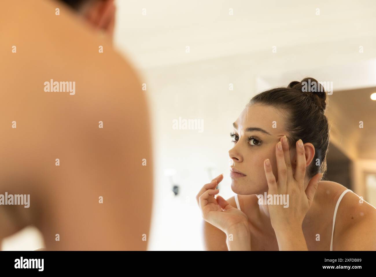 Application de soins de la peau, jeune femme regardant dans le miroir, se concentrant sur la routine de soins du visage Banque D'Images