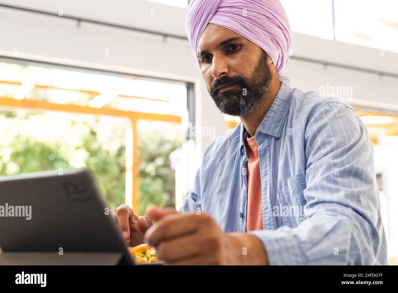 Travaillant à la maison, homme utilisant des comprimés et mangeant des repas à table Banque D'Images