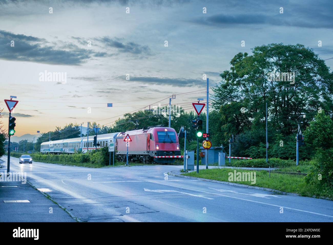 Un train de voyageurs de nuit avec locomotive rouge et autocars passe au-dessus du passage à niveau en milieu urbain à Ljubljana, Slovénie. Banque D'Images