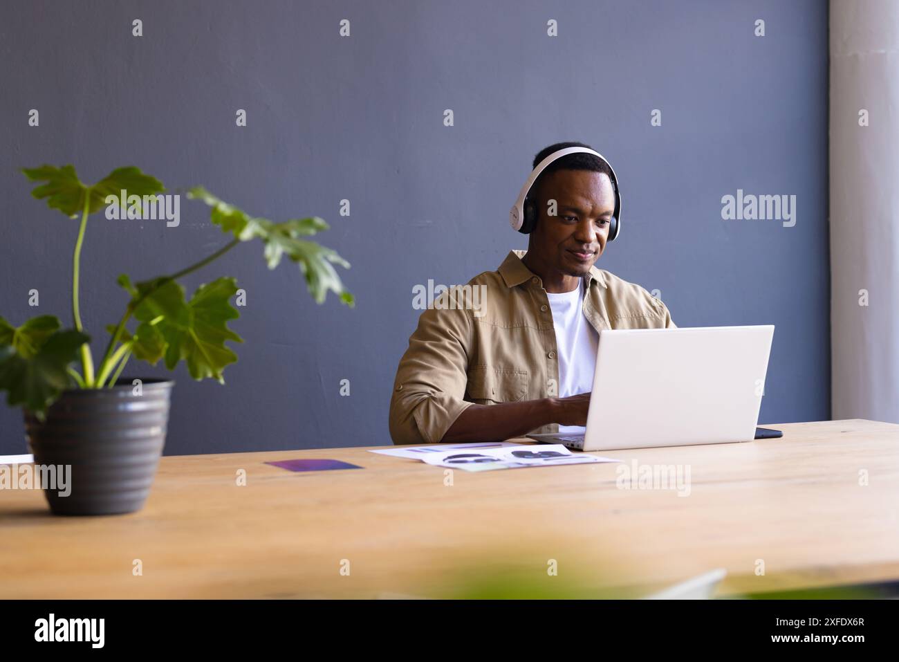 En utilisant un ordinateur portable et en portant des écouteurs, homme travaillant au bureau dans un bureau moderne Banque D'Images