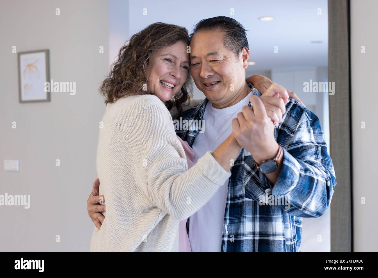 Danser ensemble, couple senior souriant dans un environnement de maison confortable Banque D'Images