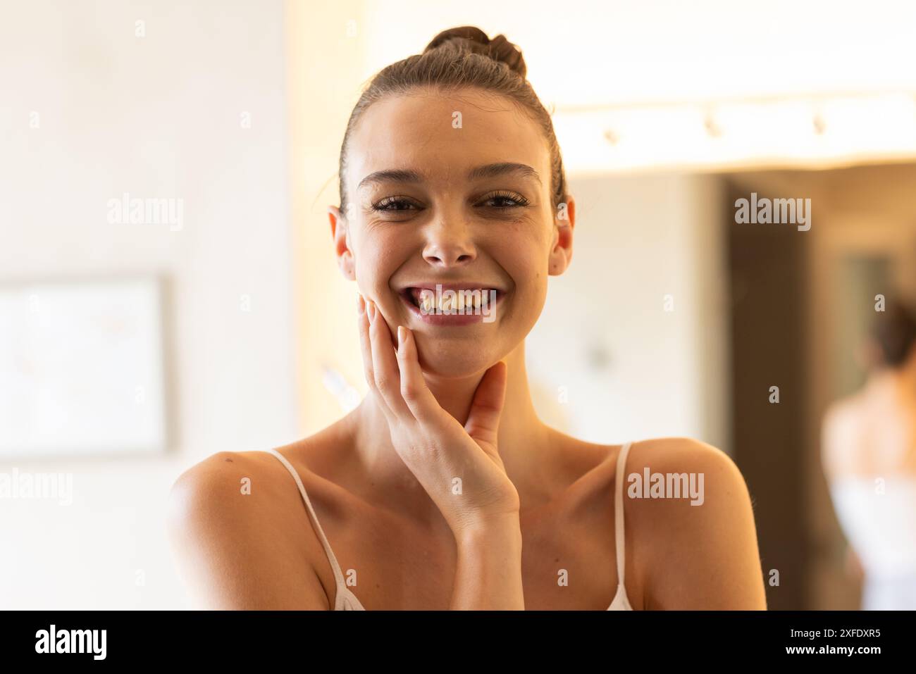 Jeune femme souriante touchant le visage, profitant de la routine matinale à la maison Banque D'Images