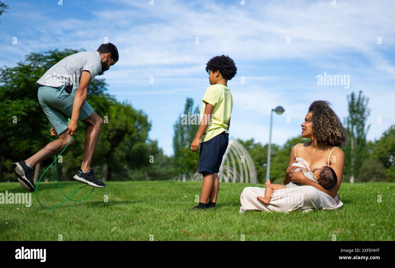 Famille latine dans un parc extérieur. Père et fils jouant et mère allaitant son bébé Banque D'Images