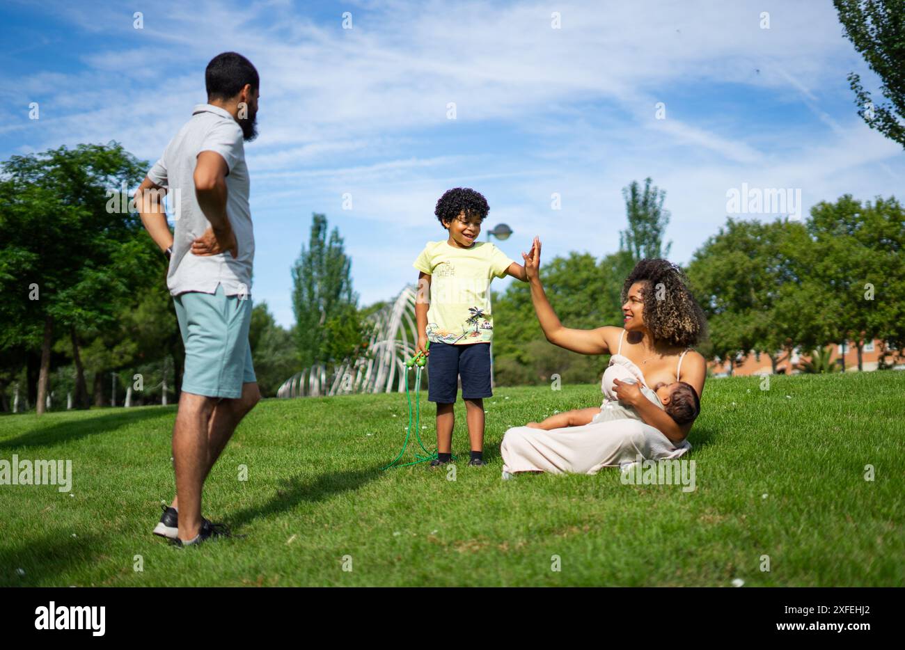 Famille latine dans un parc. Mère allaitant son bébé et donnant à son fils un grand cinq ans Banque D'Images