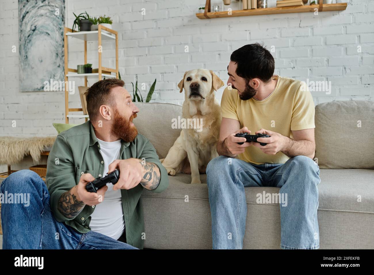 Deux hommes, profitant d'une séance de jeu sur un canapé avec une concentration intense et l'excitation pendant que leur fidèle labrador regarde de près. Banque D'Images