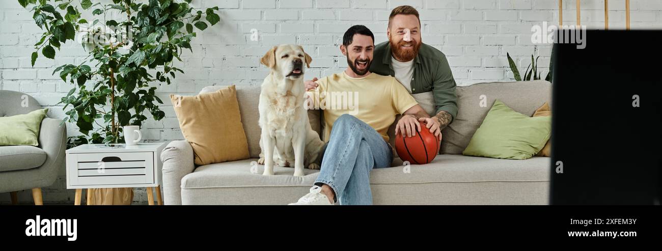 Deux hommes avec la barbe profiter du temps de qualité sur le canapé avec labrador sympathique dans le salon confortable. Banque D'Images