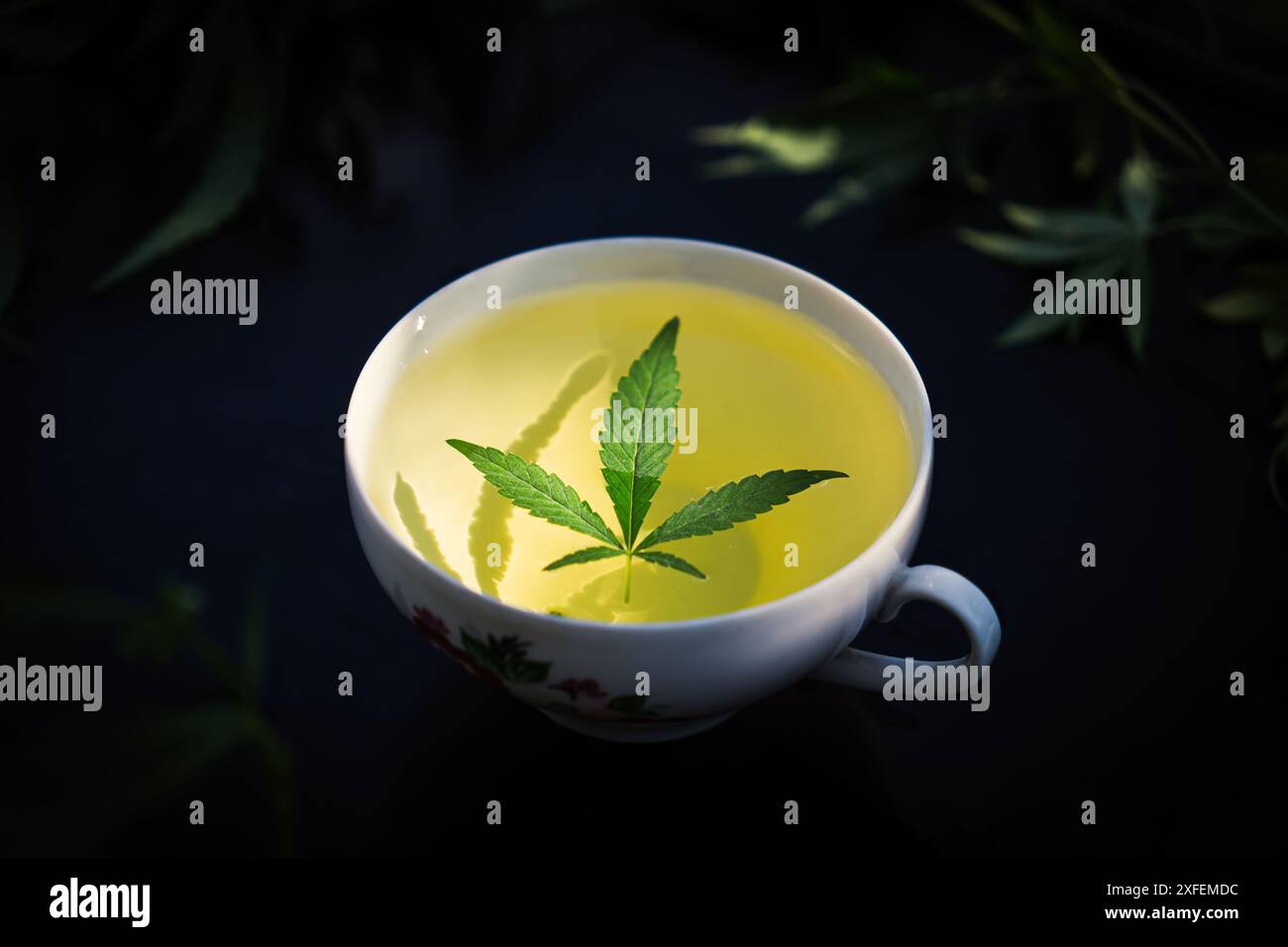 Thé de marijuana médicale. Thé de chanvre. Thé au cannabis dans une tasse de thé blanc avec une feuille de marijuana et une tige avec des fleurs et des feuilles sur une portion de Stump d'arbre en bois Banque D'Images
