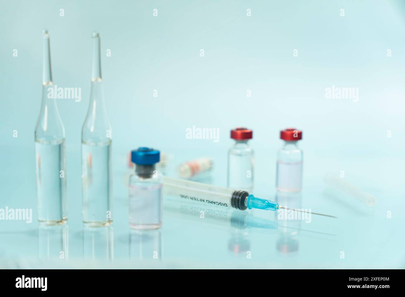 Ampoules en verre contenant du liquide à côté de la seringue avec aiguille sur la surface réfléchissante bleue, immunisation contre la maladie du virus COVID-19, vaccination à pr Banque D'Images