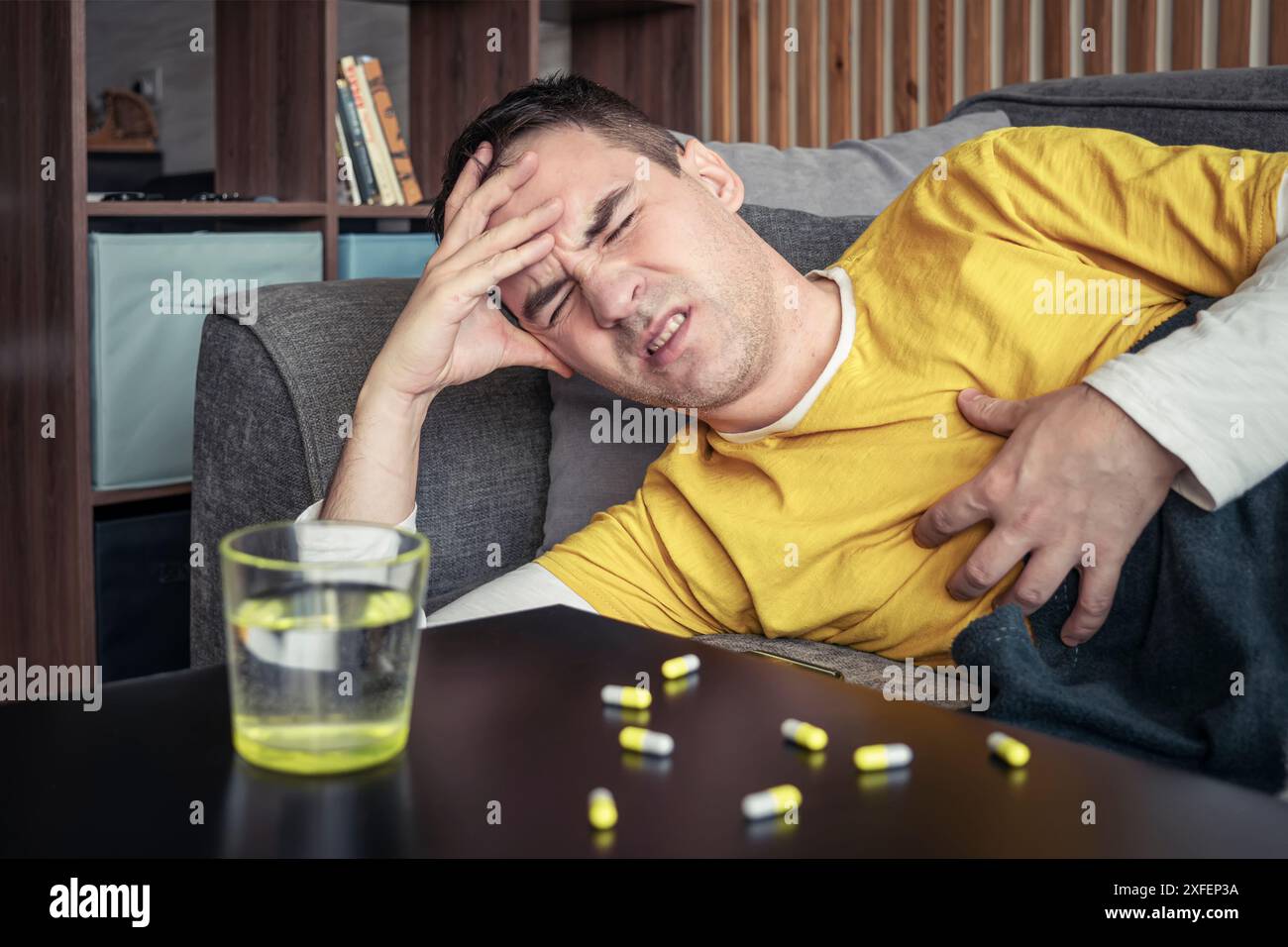 l'homme est couché avec une couverture sur le canapé à la maison pour se reposer quand il se sent malade de forte fièvre, migraine et maux de tête Banque D'Images