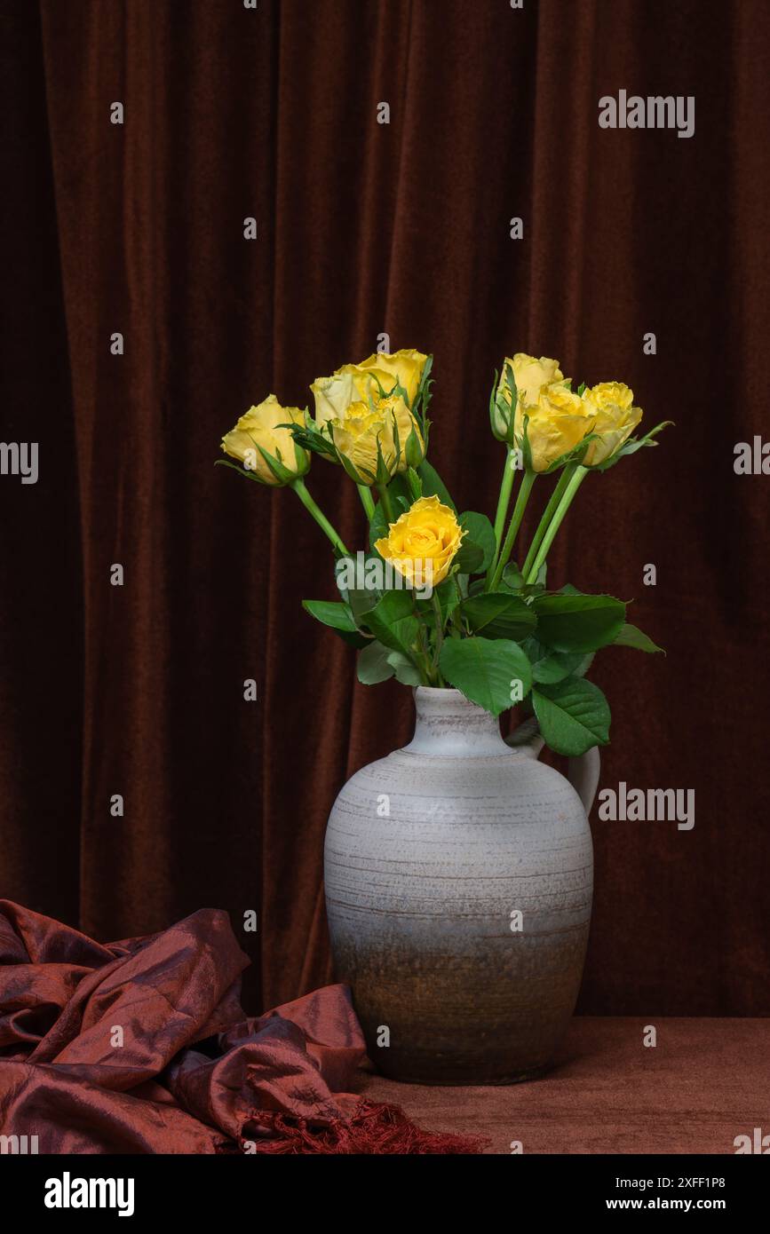 Un beau bouquet de fleurs de roses jaunes dans un vase gris sur un fond de tissu brun foncé. Placer pour le texte, copier l'espace Banque D'Images