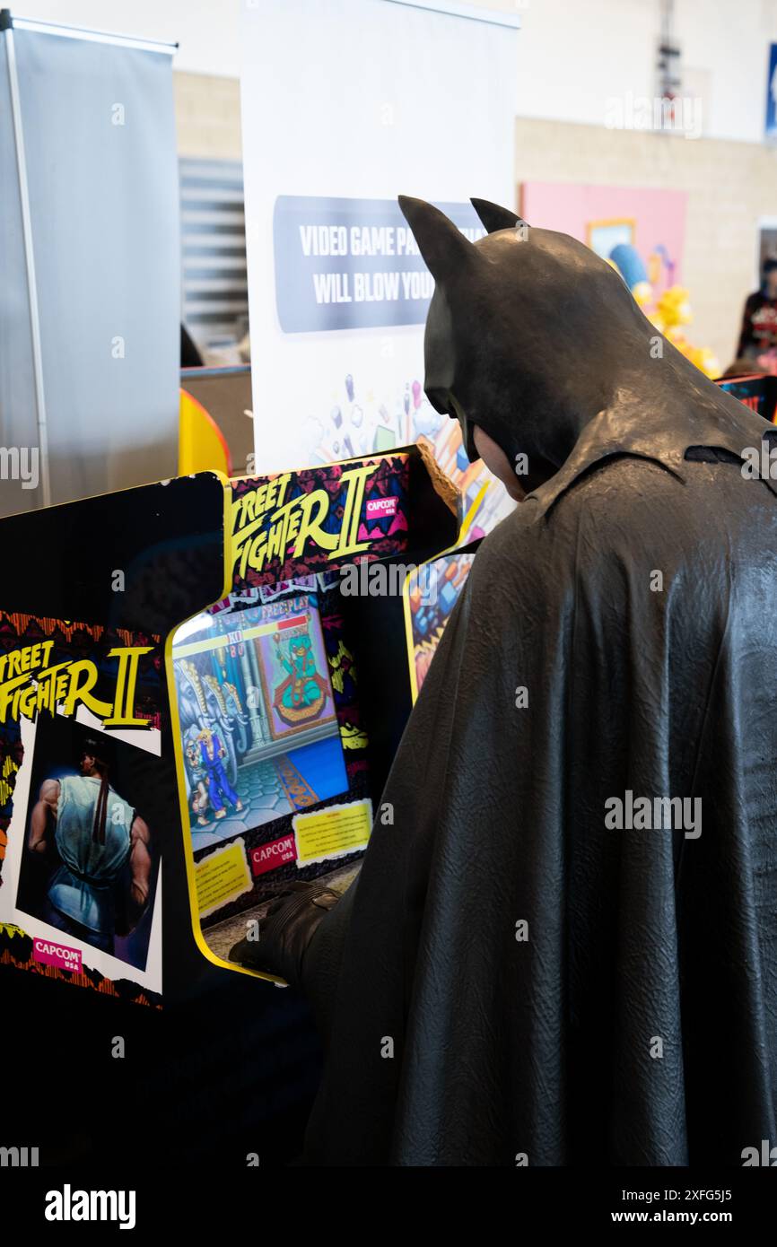 HARROGATE, ROYAUME-UNI - 22 JUIN 2024. Un cosplayer masculin habillé en Batman et jouant une console de jeux rétro de Street Fighter dans une drôle d'image de comic con Banque D'Images