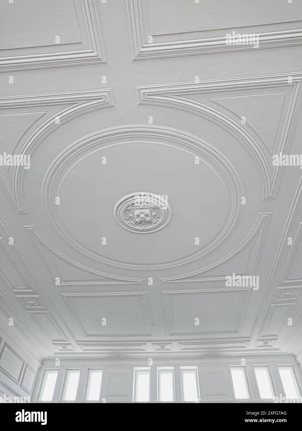Plafond blanc avec moulure décorative, lumière et espace aéré. Plafond blanc avec moulures complexes, décoration centrale et fenêtres supérieures Banque D'Images