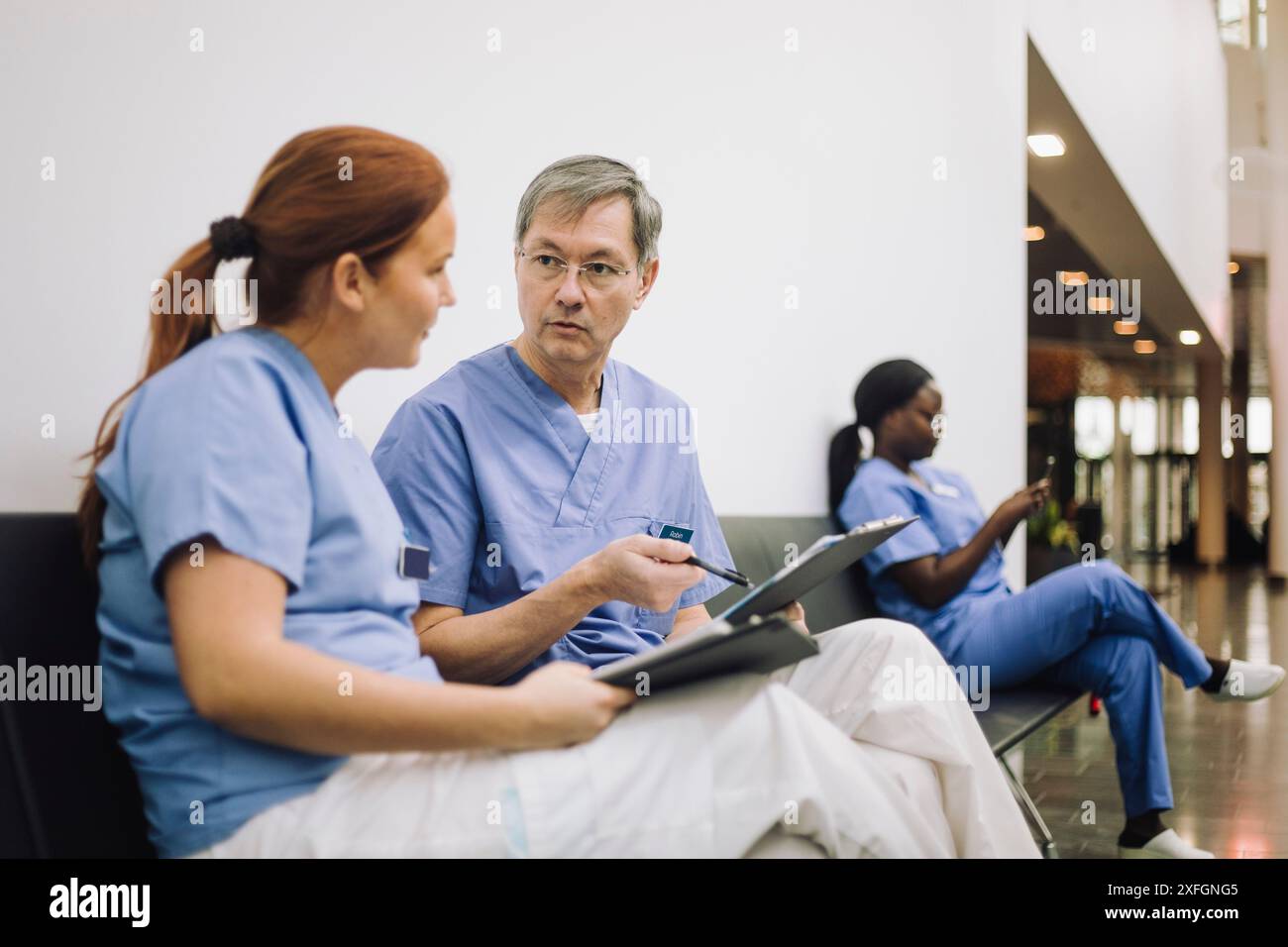 Hommes et femmes professionnels de la santé discutant tout en étant assis dans le hall de l'hôpital Banque D'Images