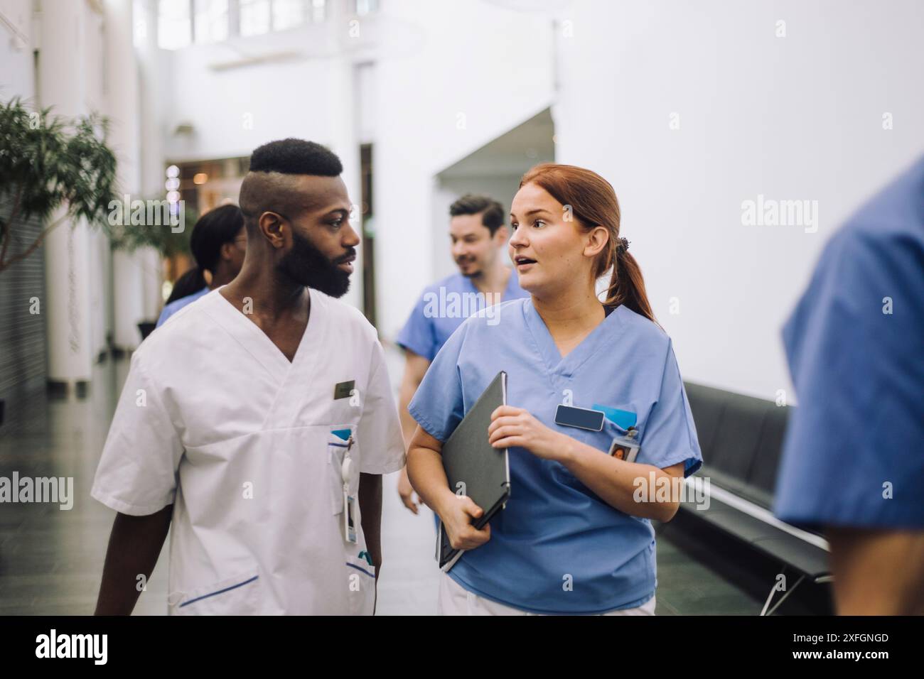Équipe d'experts médicaux masculins et féminins discutant tout en marchant dans le hall de l'hôpital Banque D'Images