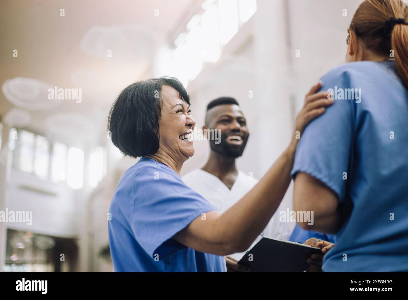 Vue latérale d'un médecin senior heureux avec la main sur l'épaule d'un collègue à l'hôpital Banque D'Images