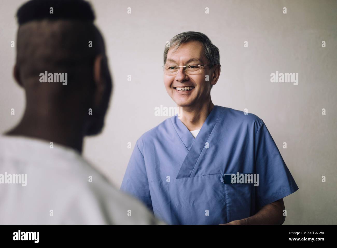Professionnel de la santé masculin souriant parlant avec un collègue près du mur Banque D'Images