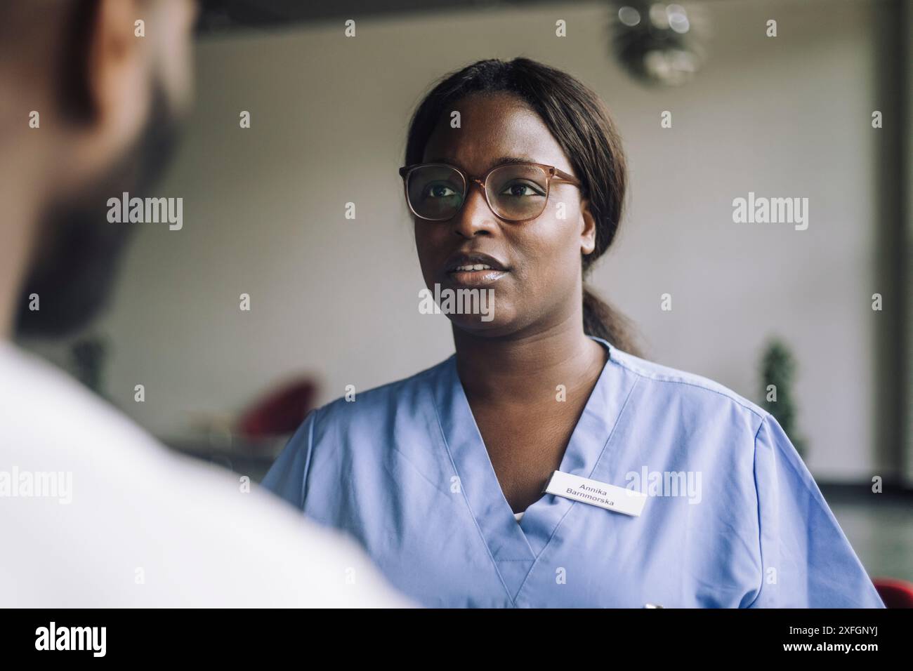 Travailleuse de santé en lunettes parlant avec un collègue masculin à l'hôpital Banque D'Images