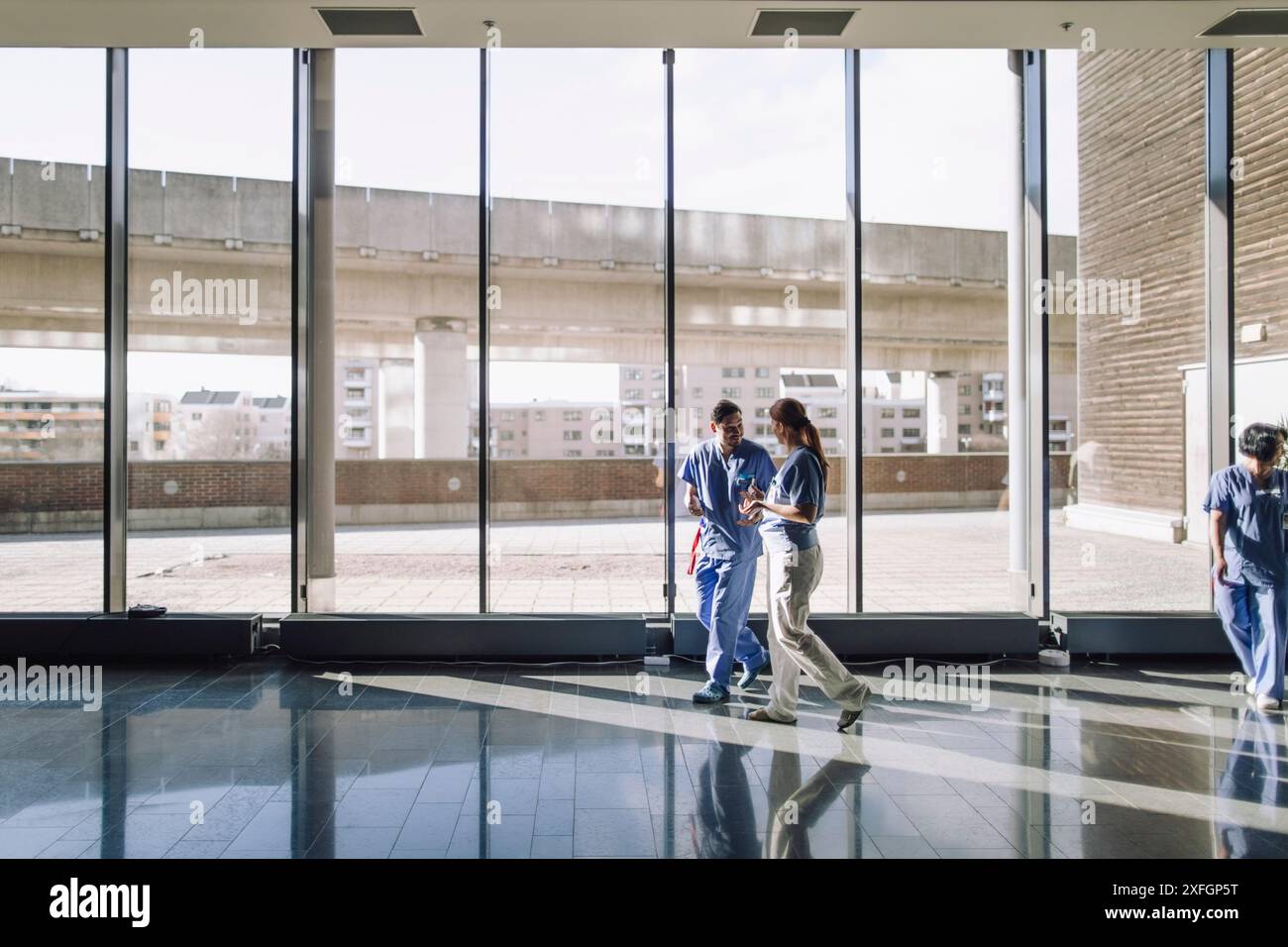 Les travailleurs médicaux masculins et féminins marchant près de la fenêtre de verre à l'hôpital Banque D'Images