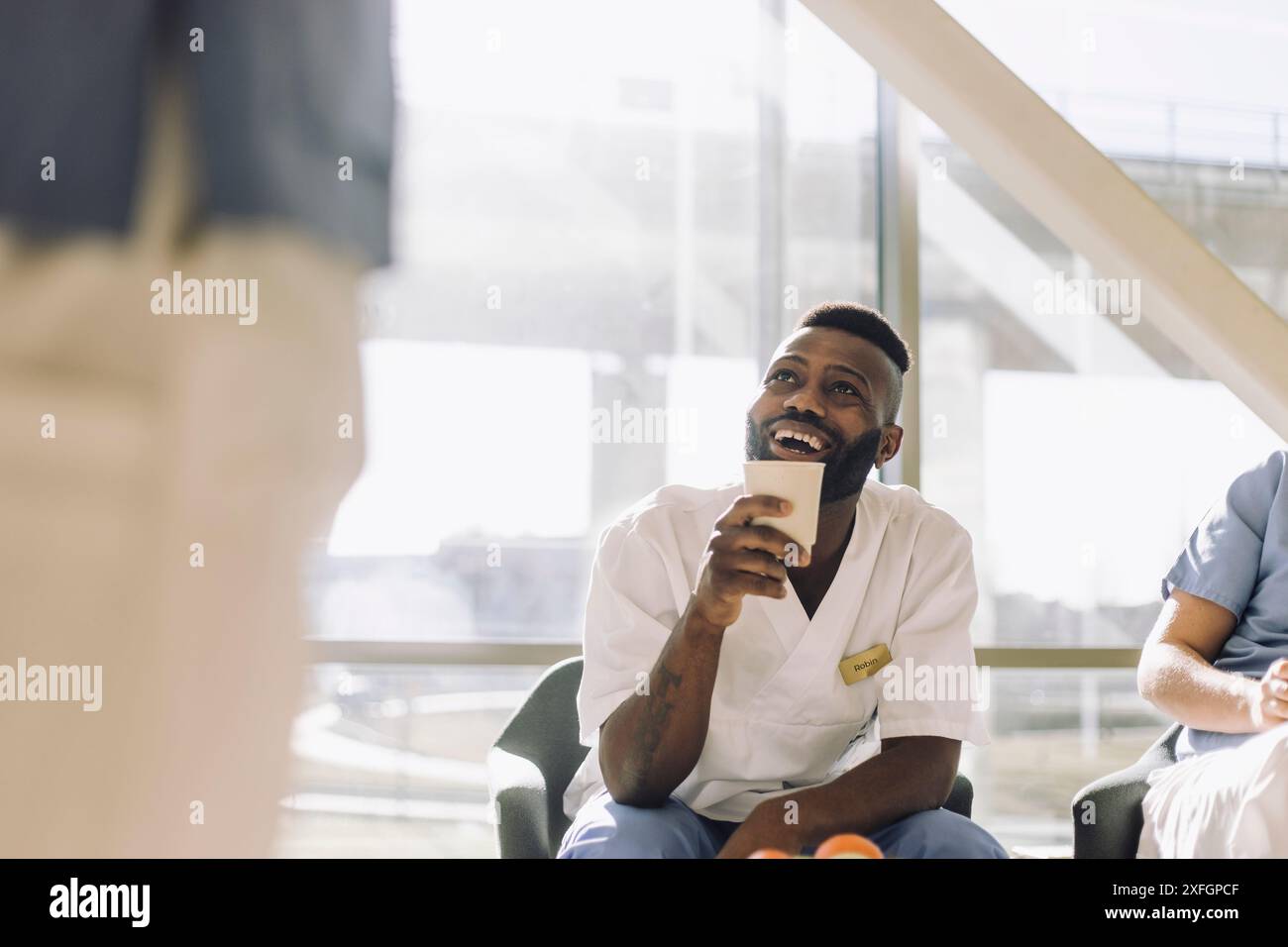 Heureux travailleur médical masculin tenant la tasse jetable tout en étant assis dans la cafétéria Banque D'Images