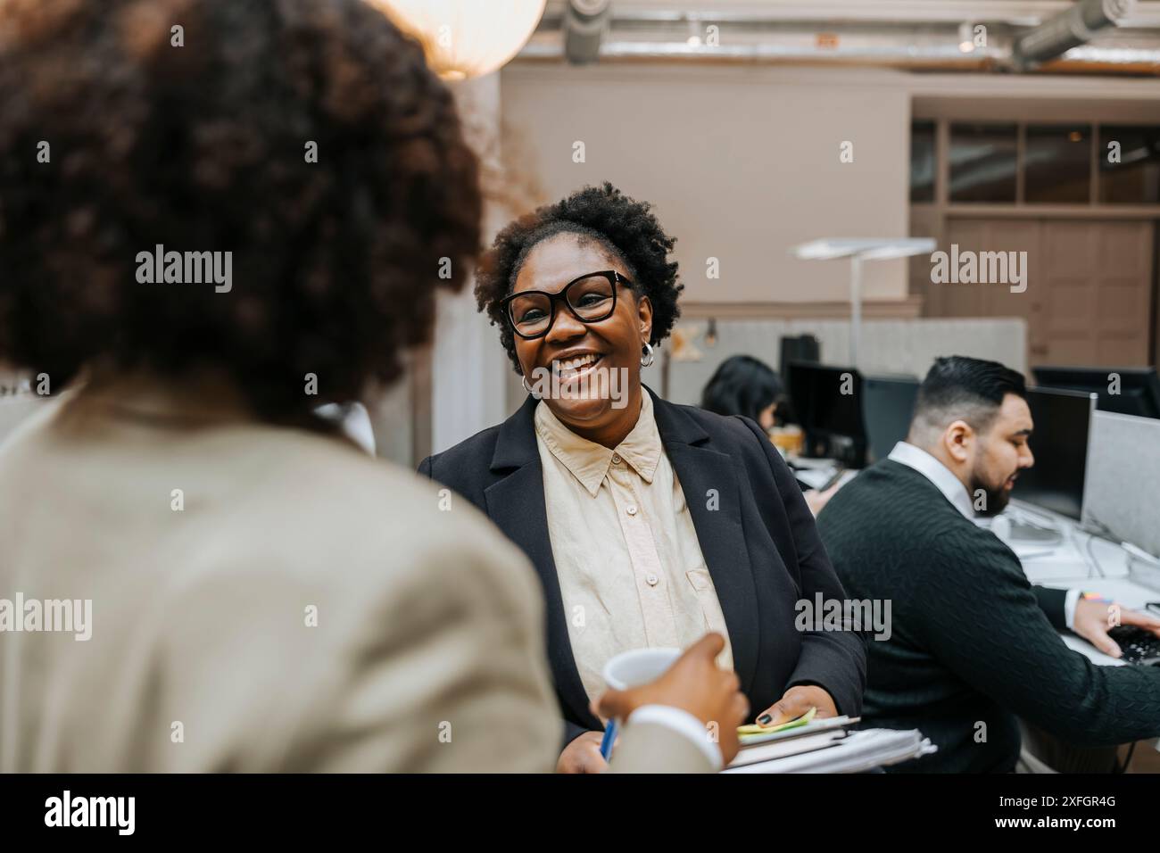 Heureuse femme d'affaires mature parlant avec un collègue tout en se tenant dans le bureau Banque D'Images