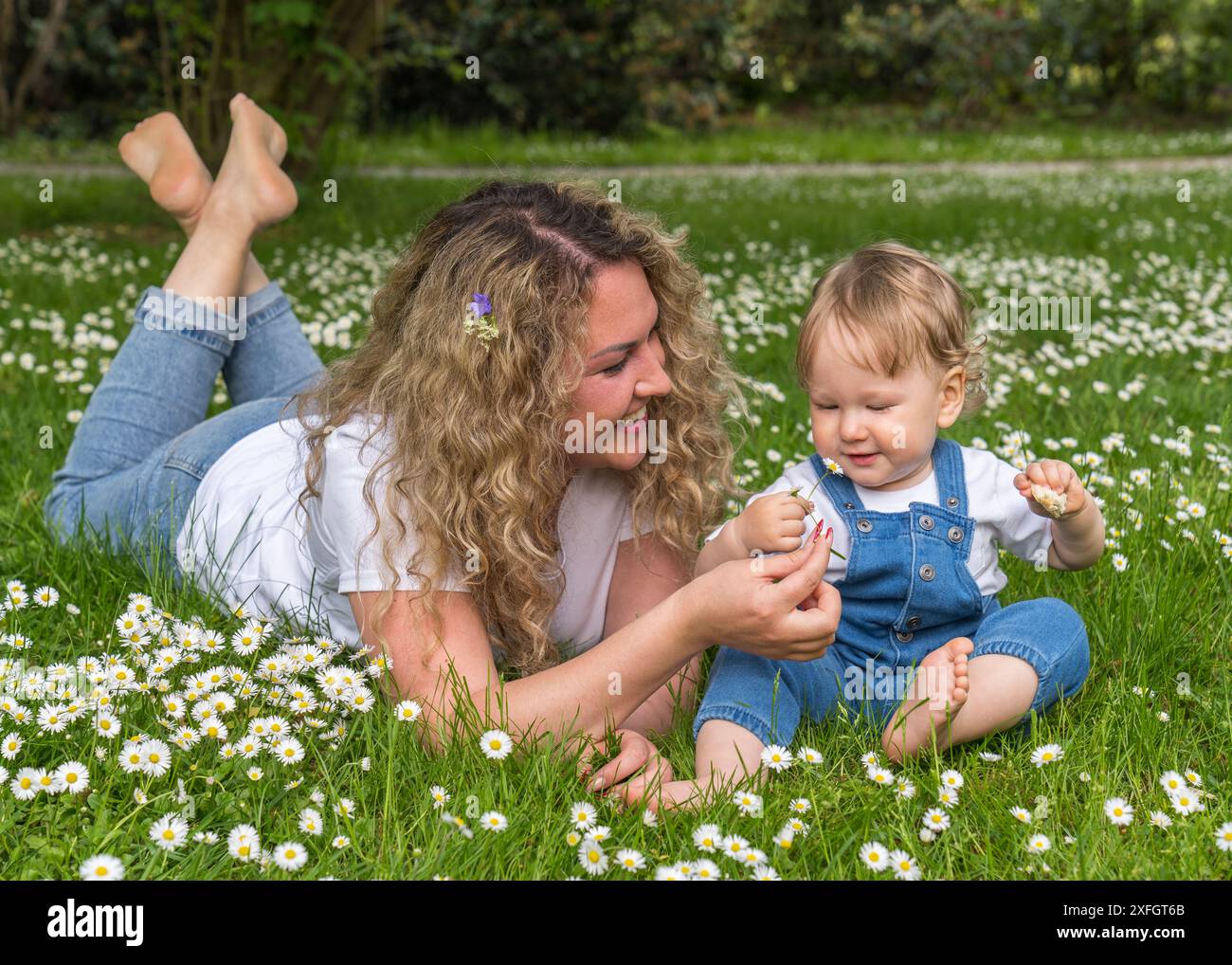 Portrait de mère et petit fils. Une mère heureuse aux cheveux ondulés se trouve sur l'herbe verte parmi les marguerites blanches, un petit bébé aux cheveux ondulés et blonds est assis Banque D'Images