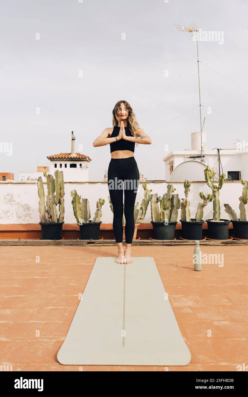 Jeune femme pratiquant la pose de prière tout en se tenant debout sur le tapis de yoga Banque D'Images