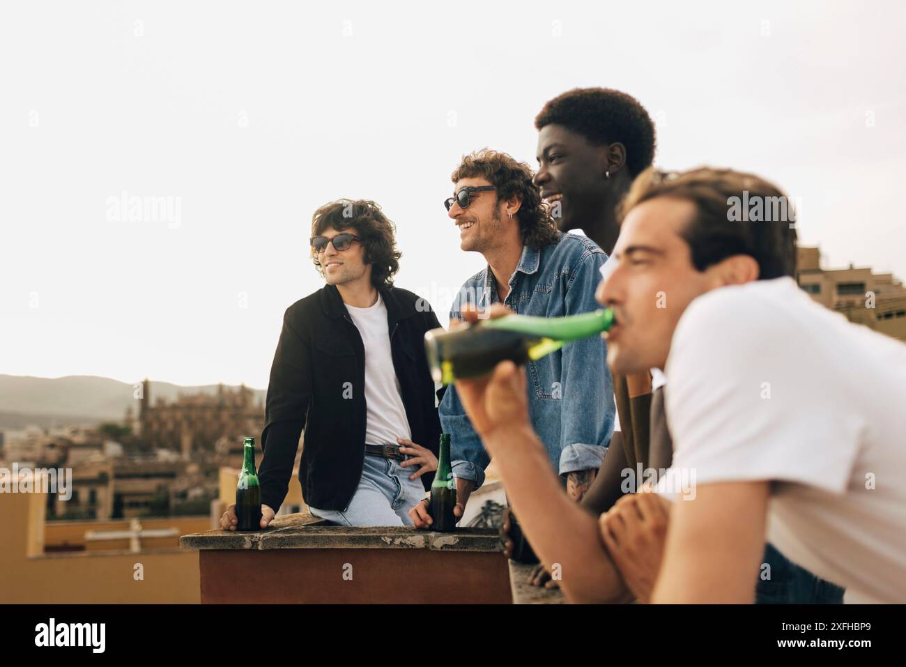 Amis masculins multiraciaux ayant de la bière pendant la fête sur le toit de construction Banque D'Images
