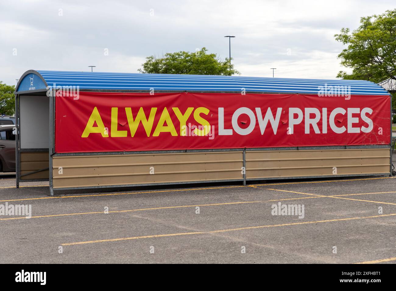 Kanata, Canada - 2 juin 2024 : toujours bas prix affiche une bannière à l'entreposage des chariots au supercentre Walmart. Aire de stationnement du grand magasin. Banque D'Images