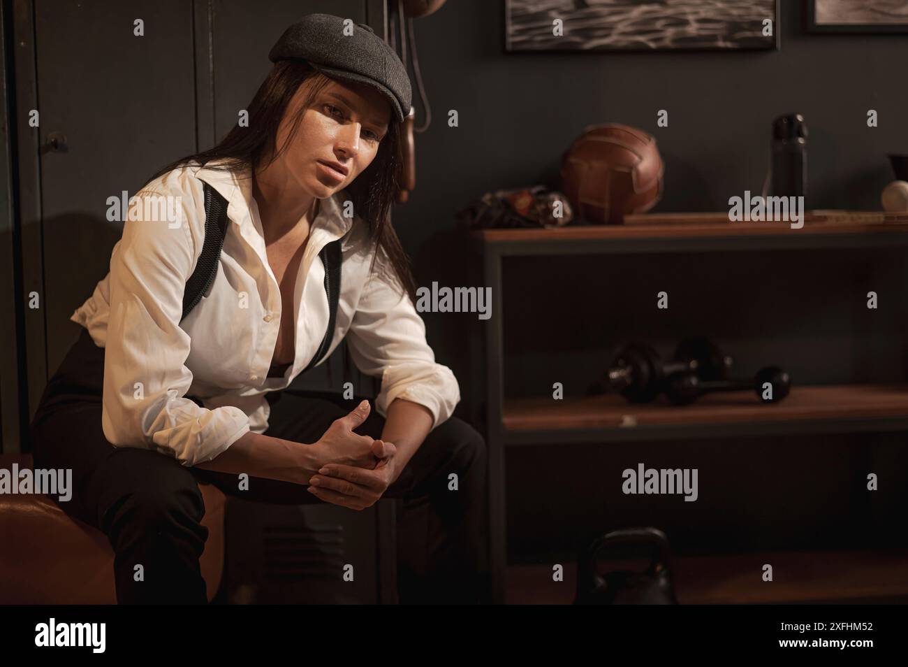 Femme caucasienne dans un costume pour hommes de style Peaky Blinders posant dans un gymnase rétro. Banque D'Images