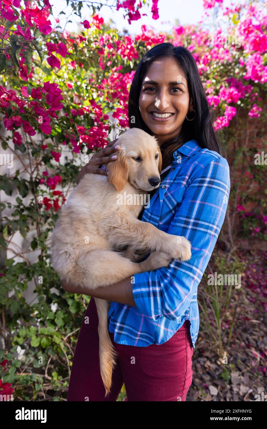 Femme souriante tenant un chiot Golden retriever dans le jardin avec des fleurs en fleurs Banque D'Images