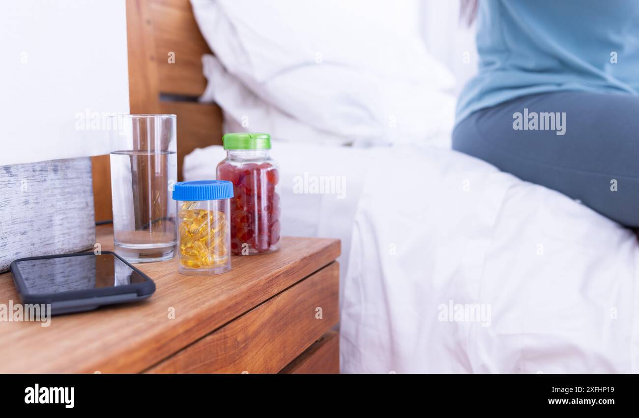 Prenant des vitamines et de l'eau potable, femme assise sur le lit dans la chambre Banque D'Images