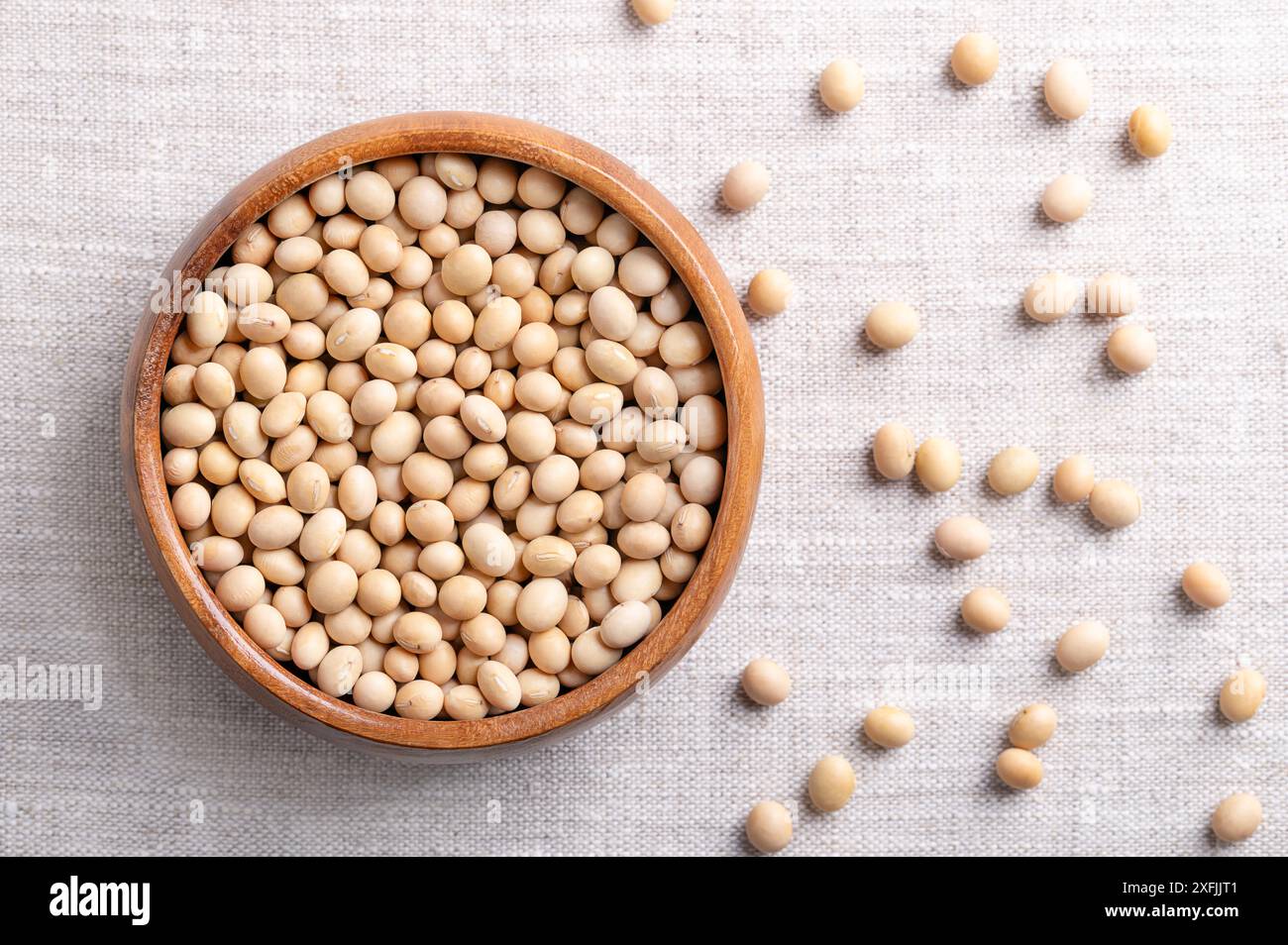 Graines de soja séchées, aussi graines de soja ou graines de soja dans un bol en bois sur tissu de lin. Graines entières et crues de légumineuses et oléagineuses Glycine max. Banque D'Images