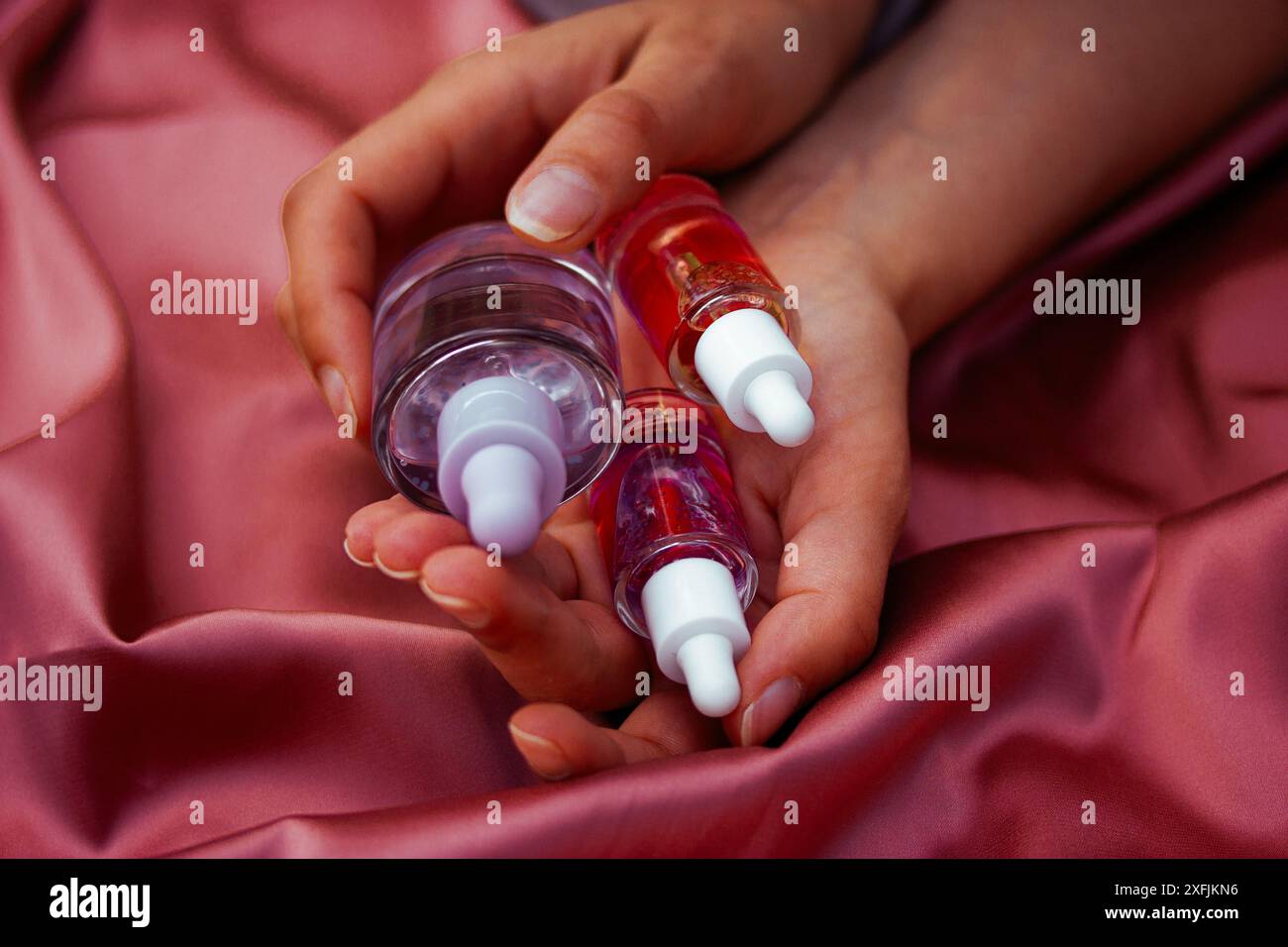 Flacons pipettes en verre transparent avec sérum pour le visage, soins du corps dans les mains féminines sur textile rose soyeux. Soins de beauté pour femmes. Produits esthéticiens. Banque D'Images