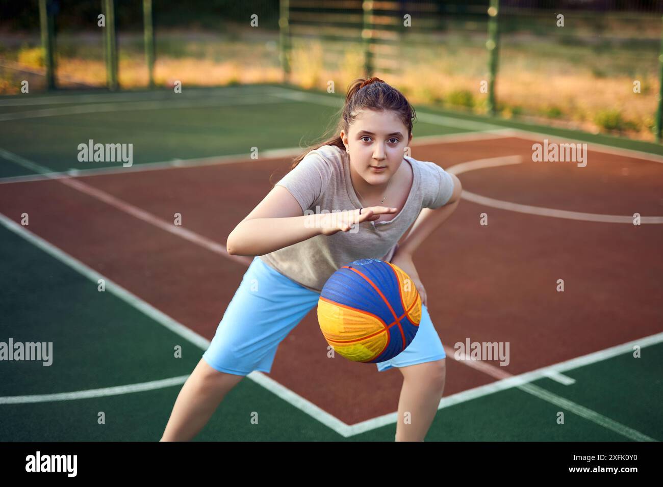 Portrait de style de vie de petite fille caucasienne joyeuse de dix ans tenant le ballon de jeu pour le basket-ball en plein air à la chaude journée d'été. Mode de vie actif, entraînez-vous Banque D'Images