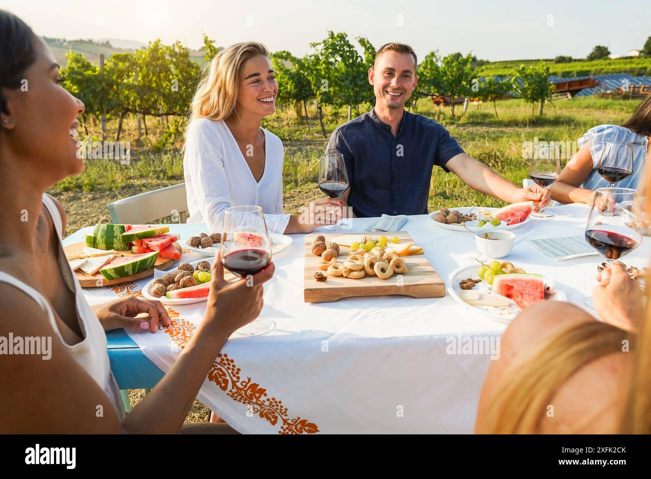 Amis multiraciaux buvant du vin rouge et mangeant avec le vignoble en arrière-plan - personnes multiraciales faisant la dégustation de vin à l'heure d'été dans le comptr Banque D'Images