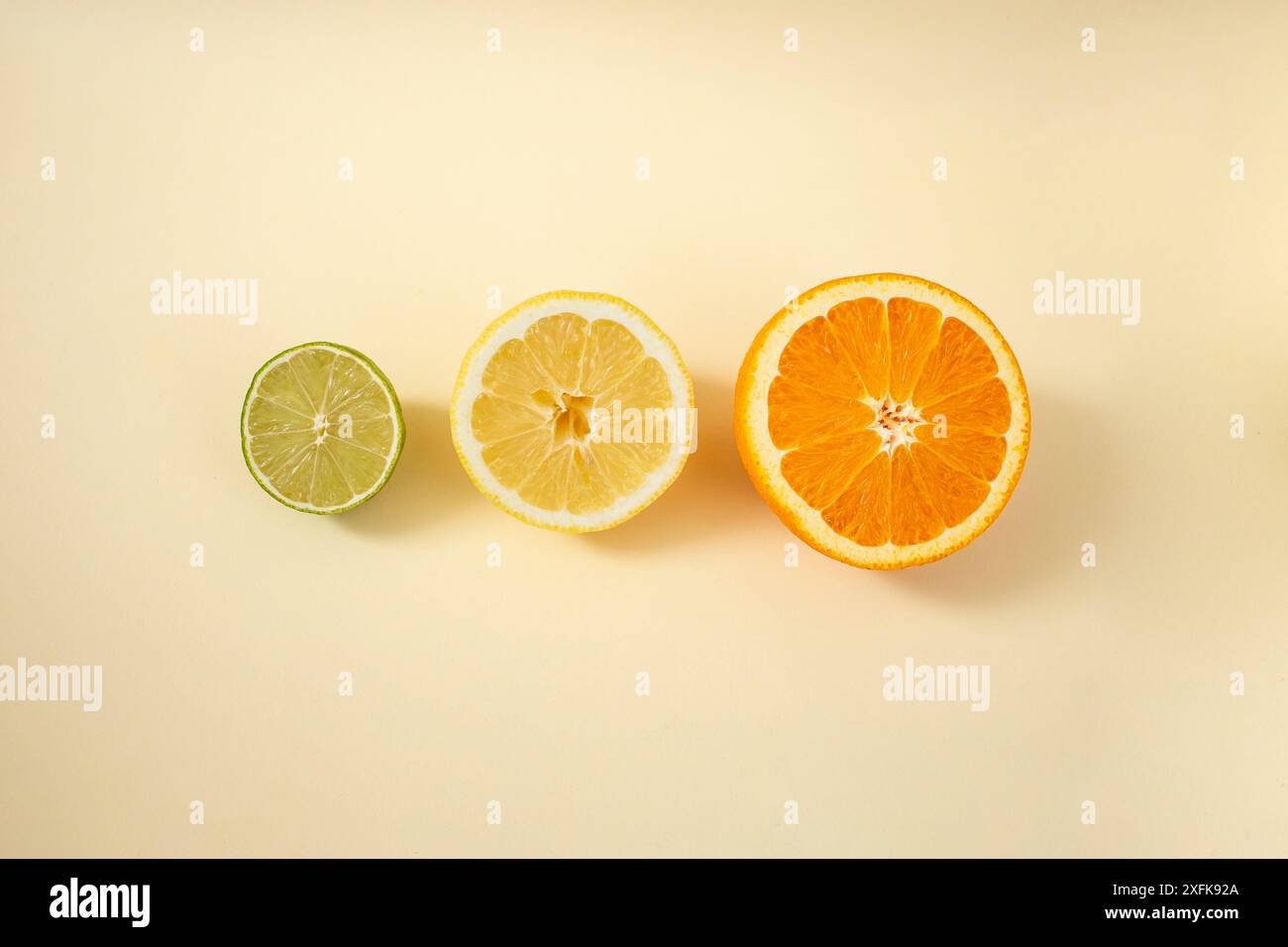 Citron vert, citron et moitiés orange disposées sur fond beige, pose à plat Banque D'Images