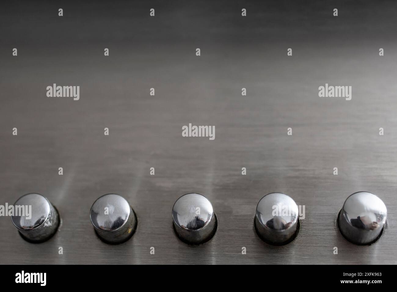 Cinq boutons en acier inoxydable sur fond métallique gris, texture abstraite avec espace de copie Banque D'Images