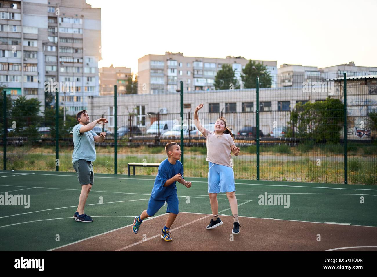 Motion shot d'un père heureux et d'enfants jouant au basket-ball ensemble à l'extérieur sur un terrain de basket-ball moderne parmi des maisons ordinaires, dans une zone urbaine Banque D'Images