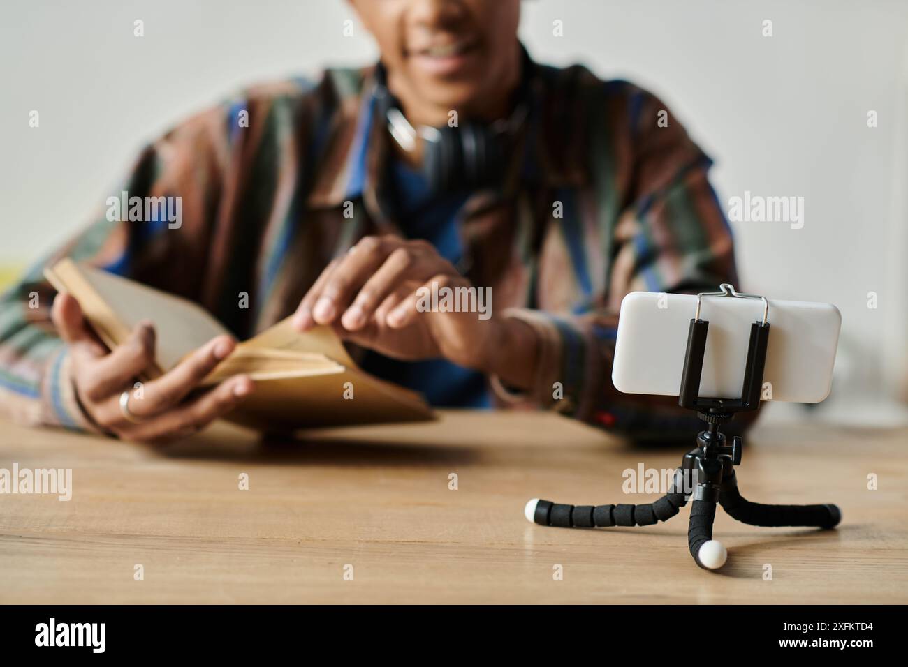 Homme afro-américain lit le livre tout en vlogging sur le trépied du téléphone. Banque D'Images