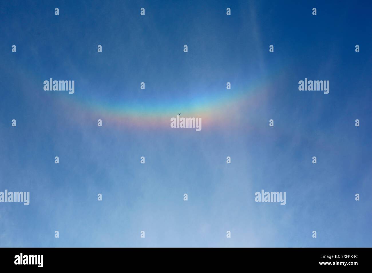 Le jet liner passe sous un « arc nuageux » causé par des cristaux de glace dans les nuages élevés réfractant la lumière du soleil couchant. Surrey, Angleterre, Royaume-Uni, avril. Banque D'Images