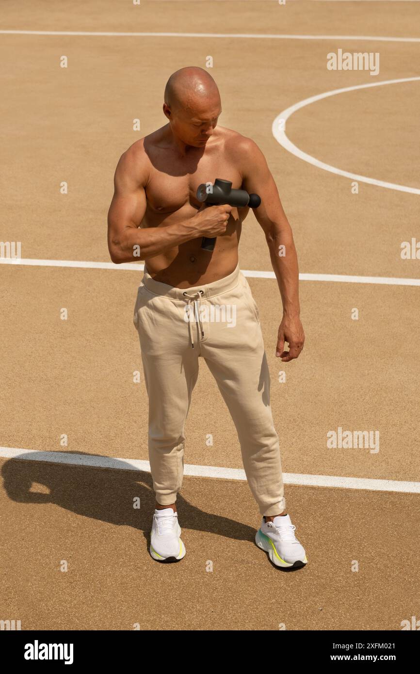 Homme sportif bronzé massant les muscles de la poitrine après l'entraînement. Pistolet de massage pour athlètes, percussion professionnelle sans fil portable corps profond de tissu musc Banque D'Images