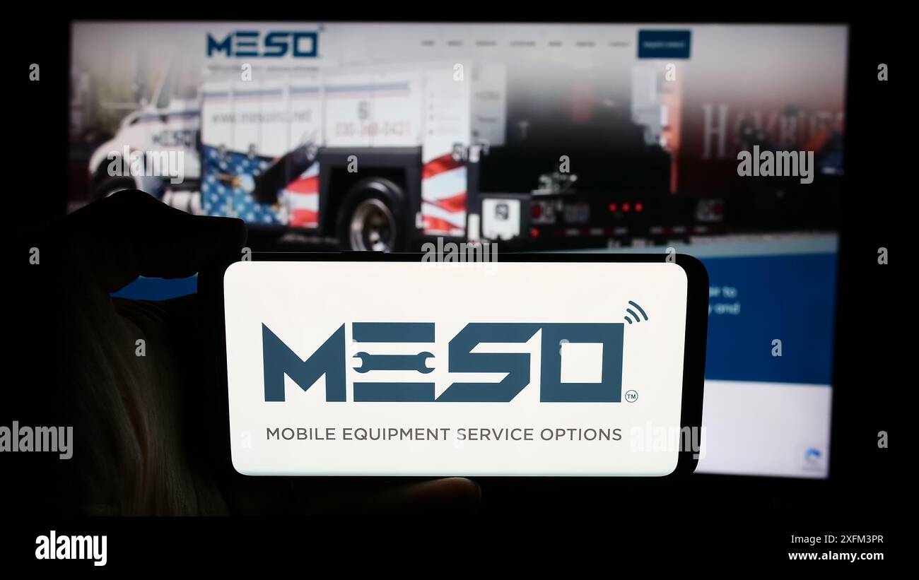 Personne tenant le téléphone portable avec le logo de la société de services de maintenance US MESO Inc en face de la page Web de l'entreprise. Concentrez-vous sur l'affichage du téléphone. Banque D'Images