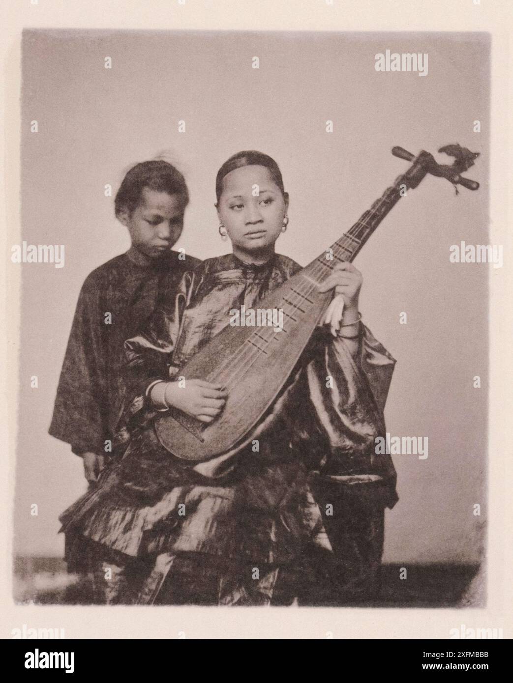 Photo vintage de musicain chinois avec jeune garçon. Illustration de la Chine Qing, 1875 illustration représentent la guitare chinoise, avec les interprètes, qui sont embauchés à des occasions festives. Les Chinois ont un certain nombre d'airs plaintifs et agréables qu'ils chantent ou interprètent sur leurs instruments à cordes et à vent. Banque D'Images