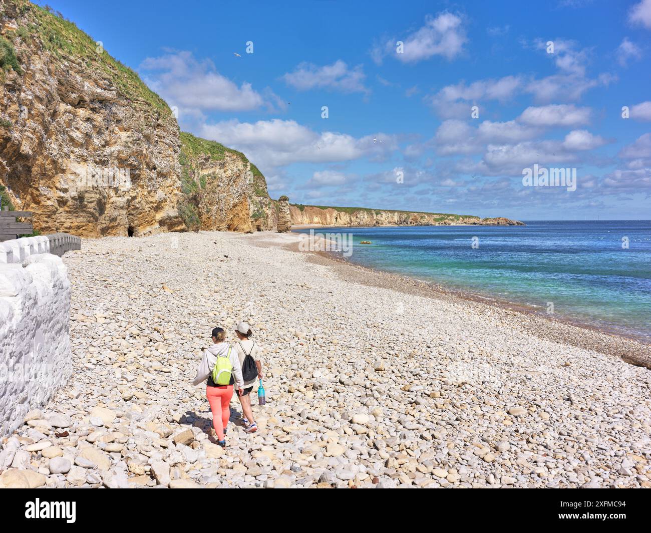 Couple sur la plage de galets près des falaises et une mer du Nord calme au large de la côte anglaise à South Shields, Angleterre. Banque D'Images