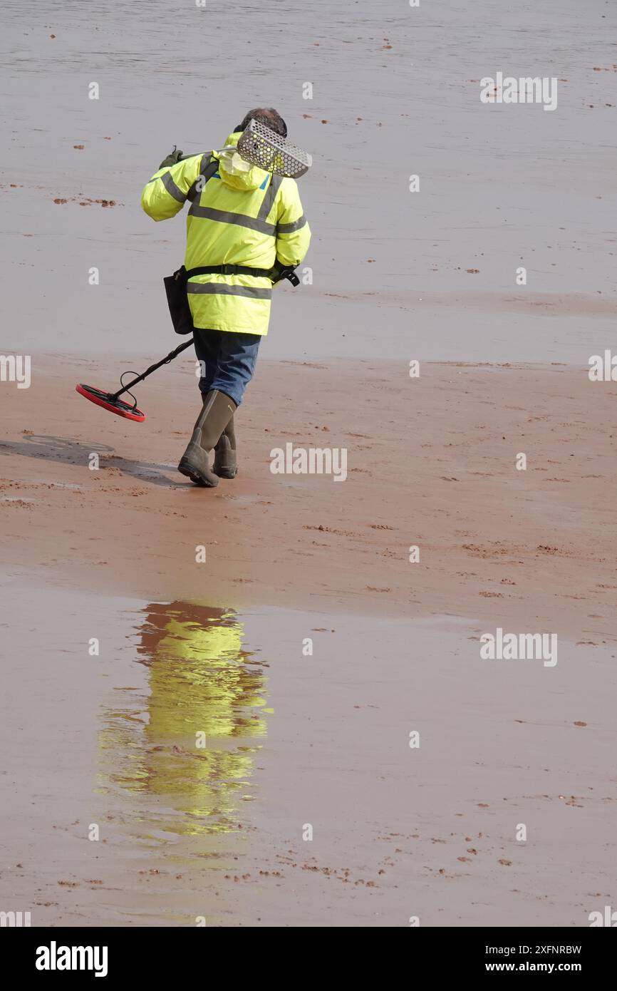 Un homme utilisant un détecteur de métaux pour rechercher des objets perdus sur une plage vide Banque D'Images