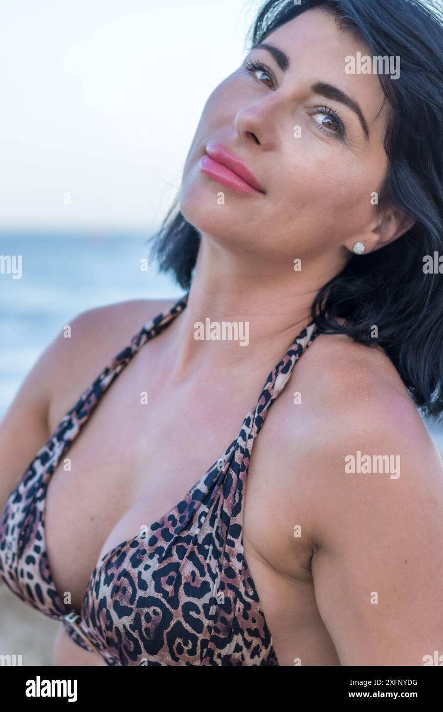 Cette image capture un moment radieux sur une plage ensoleillée. Une femme brune dans un maillot de bain se tient sur le shor sablonneux Banque D'Images