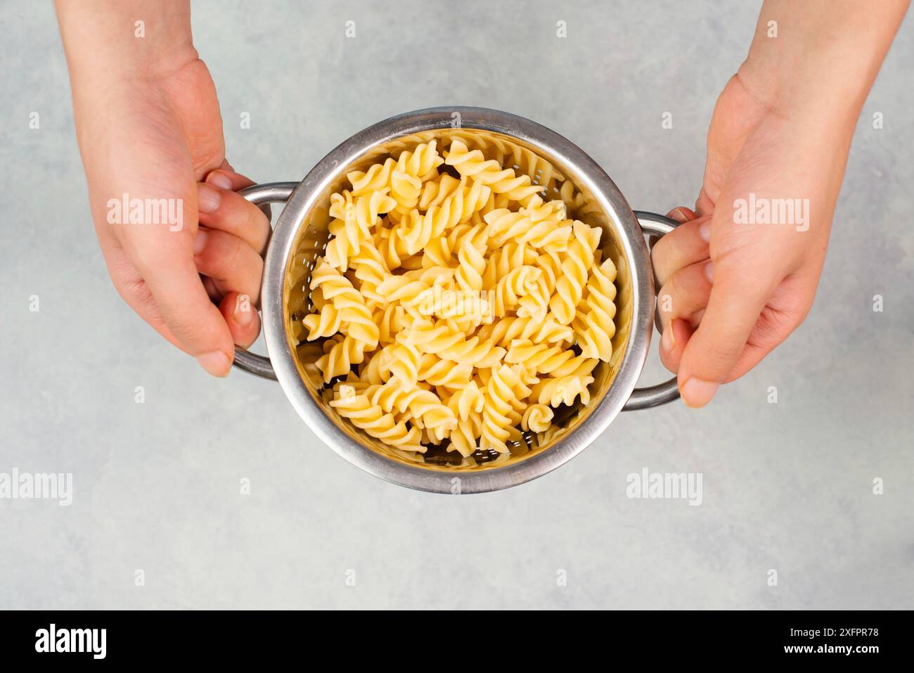 Pâtes fusilli cuites dans un tamis ou une passoire, ingrédients alimentaires italiens, mains tenant une passoire Banque D'Images